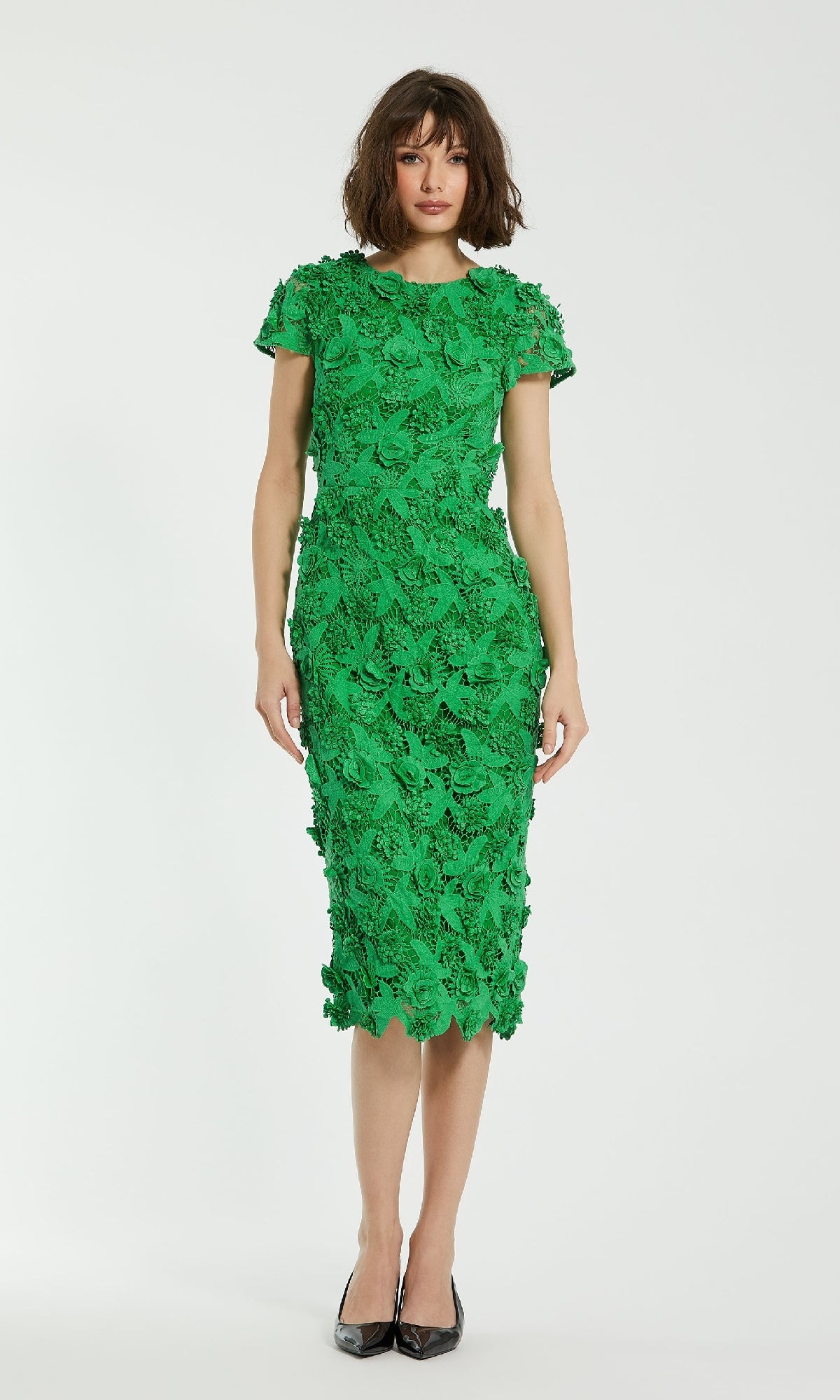 A woman poses against a white background wearing the Mac Duggal 81022 Midi Lace Cocktail Dress in green, featuring a textured finish, short sleeves, and black pointed-toe heels.